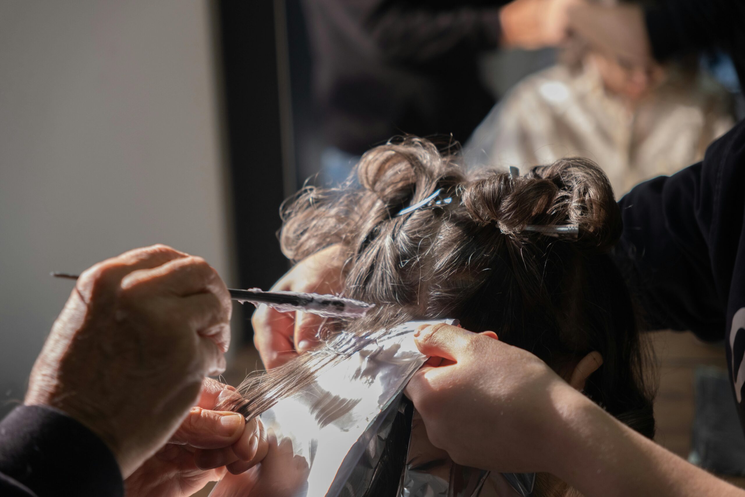 Profesional aplicando producto de coloración en un mechón con papel de aluminio durante un servicio de mechas.